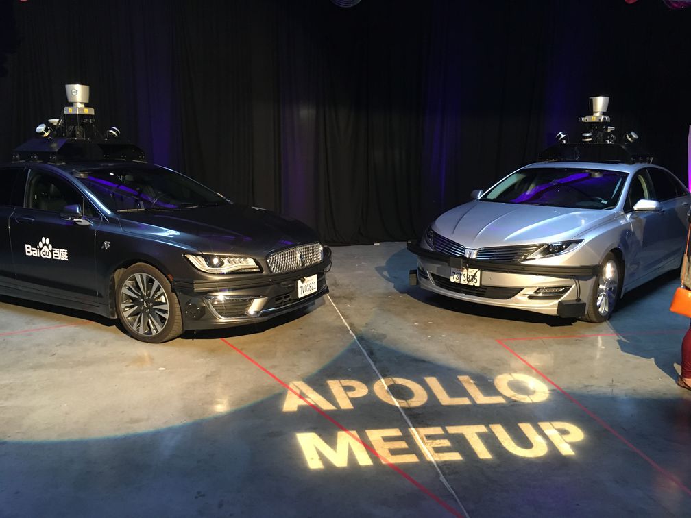 Two autonomous vehicles in spotlights with Apollo Meetup projected on floor